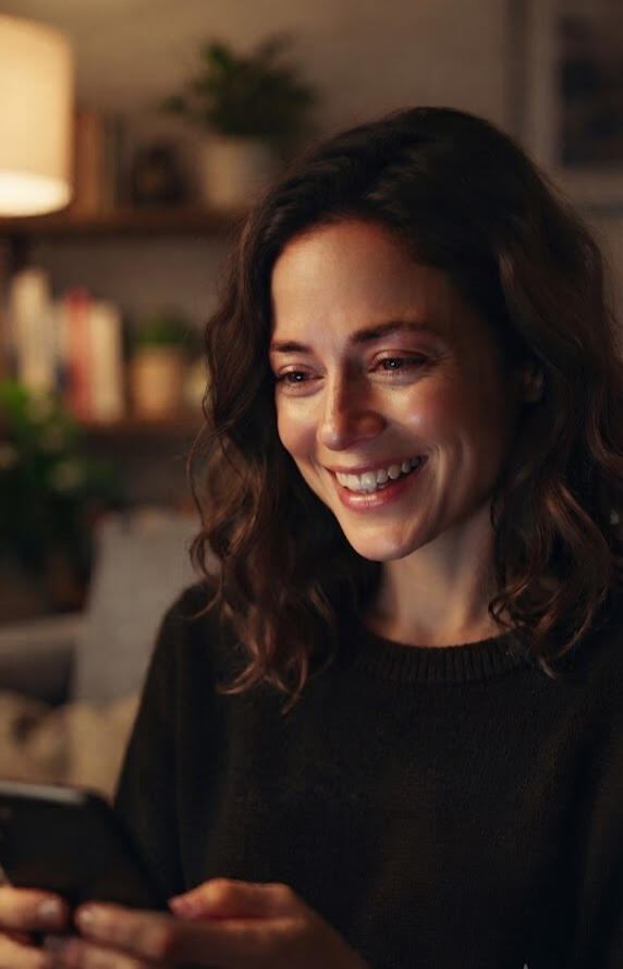 Custom poetry gift reaction A woman smiling warmly while watching a personalized custom poetry video on her smartphone at home.